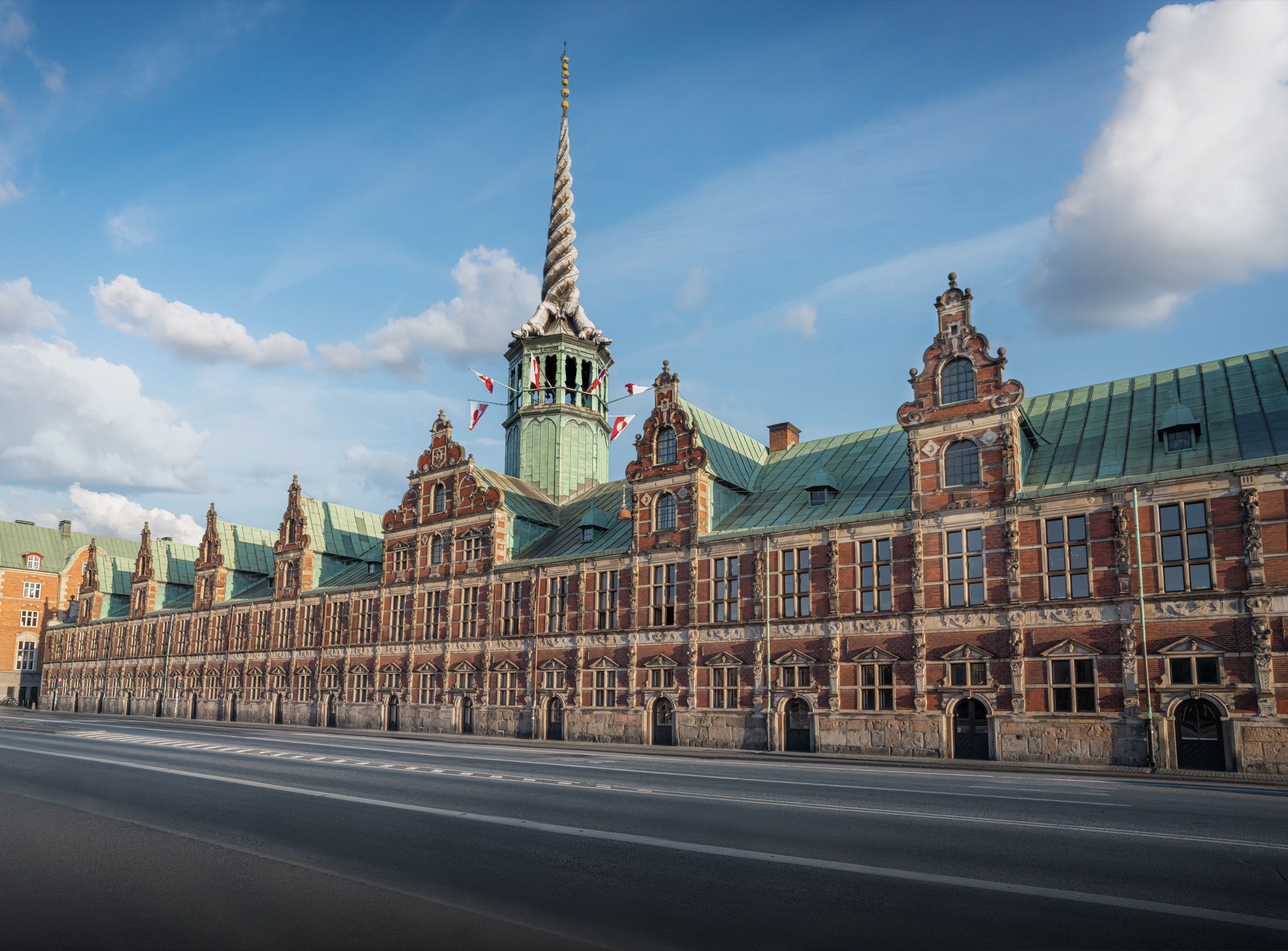 Die prachtvolle Boerse von Kopenhagen mit dem charakteristischen Drachenspiraturm ragt hinter dem roten Backsteingebaeude in den blauen Himmel.