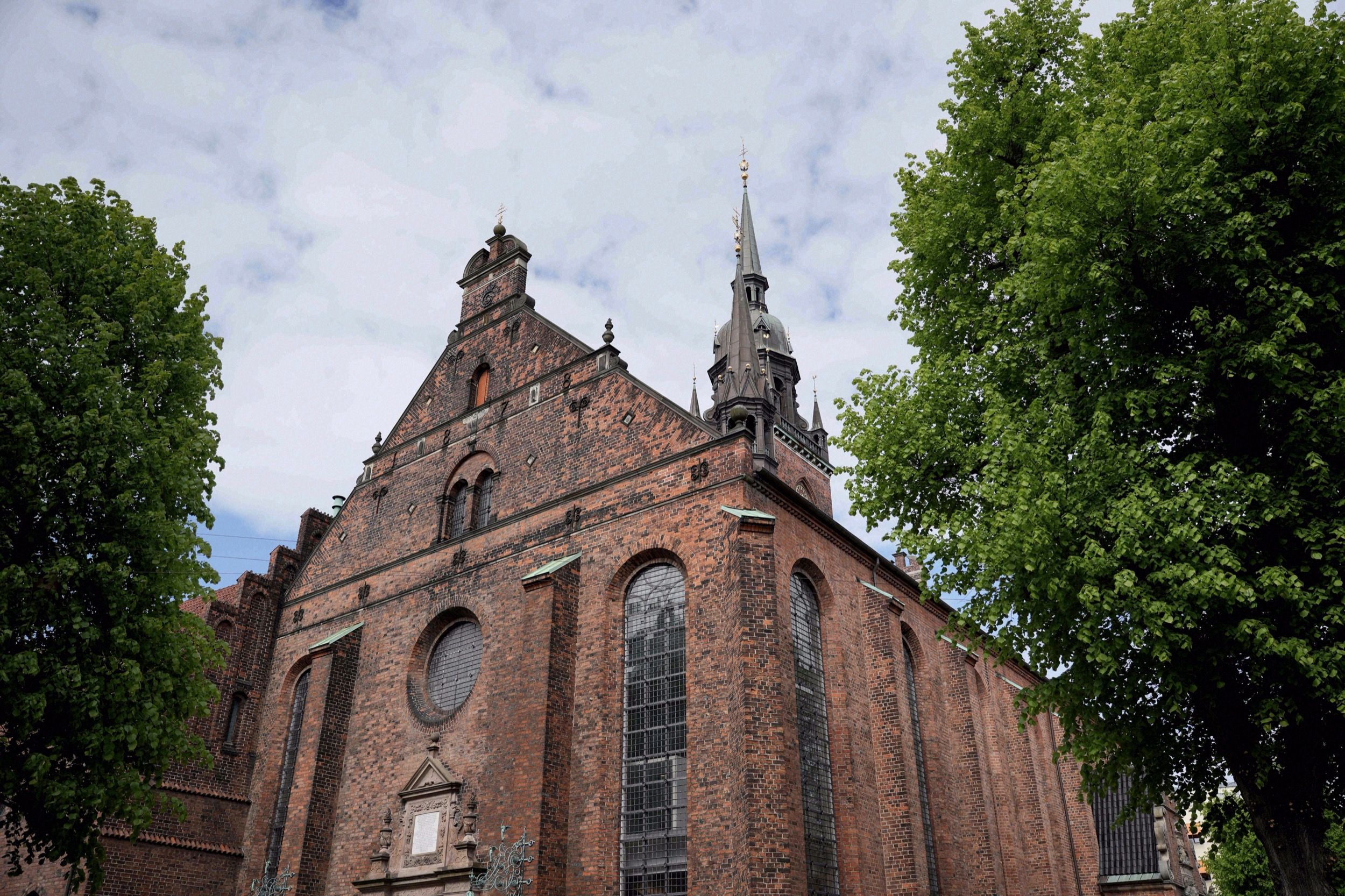 Die mächtige Backsteinfassade der Helligaandskirken (Kirche des Heiligen Geistes) in der Kopenhagener Innenstadt, gerahmt von sommerlichen Baeumen.
