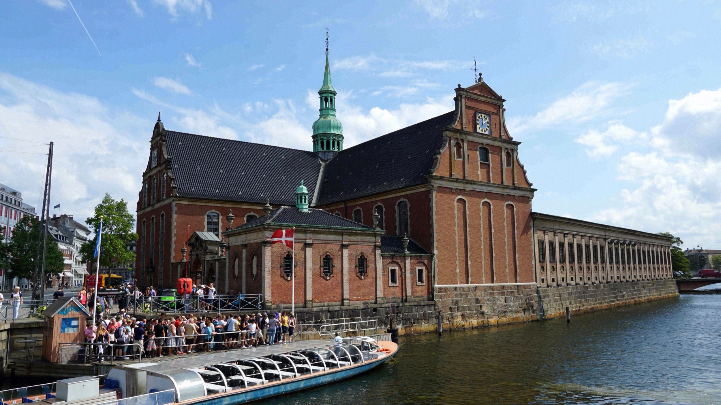 Holmens Kirke am Slotsholmskanal mit Touristenboot und dänischer Flagge im Vordergrund.