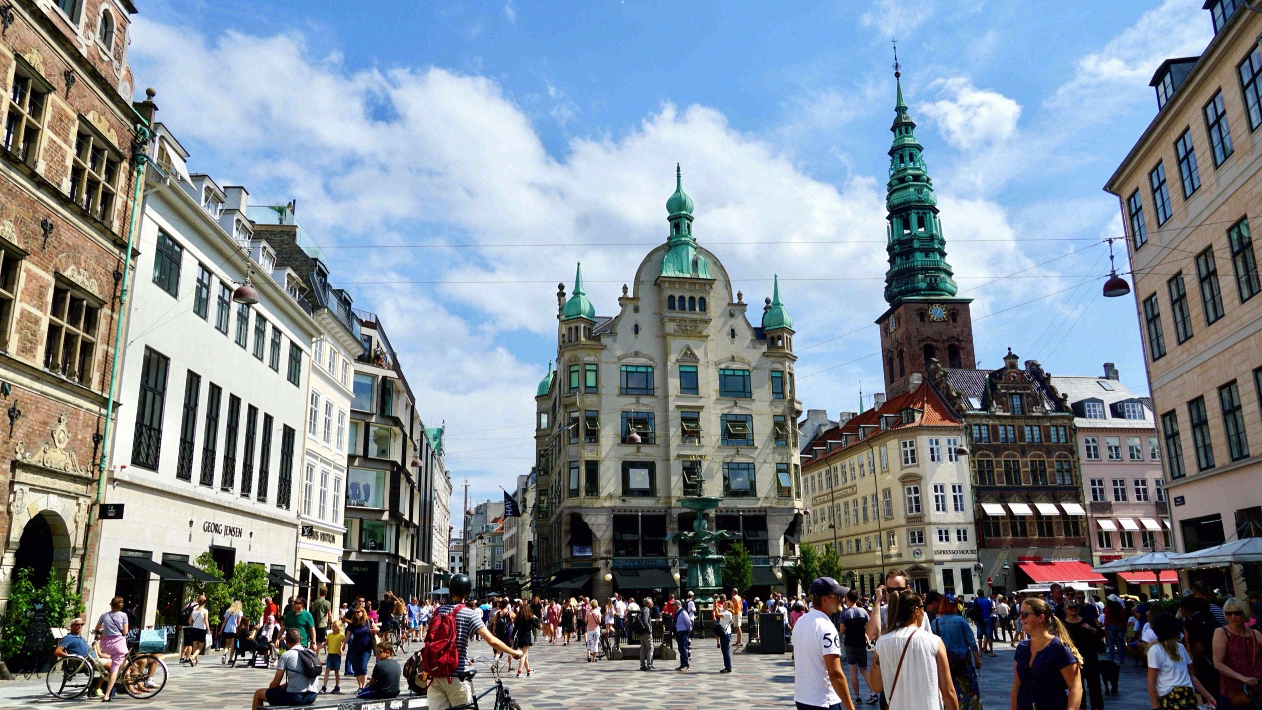Der Storkespringvand (Storchenbrunnen) auf dem belebten Amagertorv mit Blick auf die Fussgaengerzone und den Nikolaj-Kirchturm im Hintergrund.