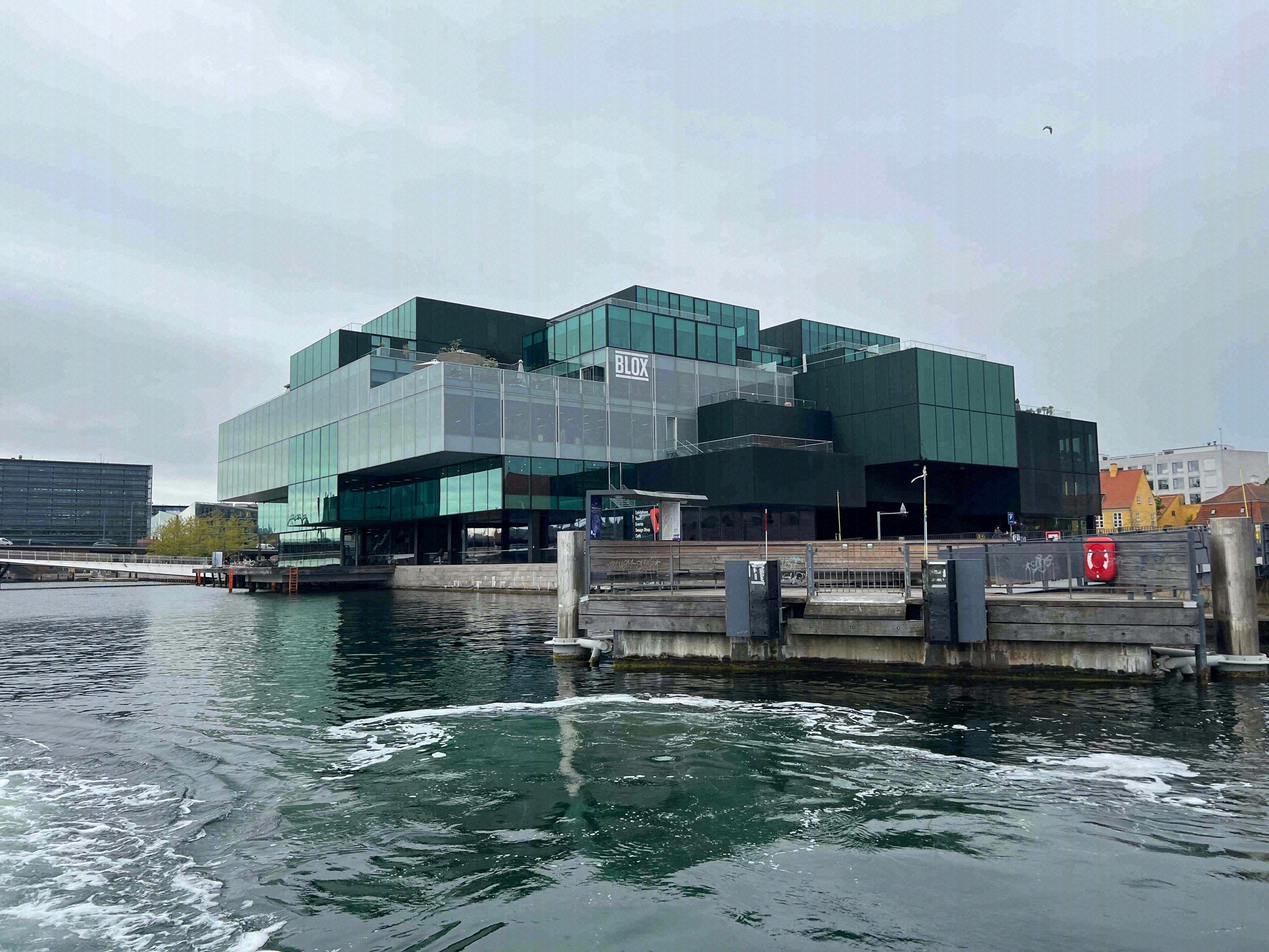 Das markante BLOX-Gebaeude (Danish Architecture Center) mit gruener Glasfassade und gestapelten Baukoerpern, von der Hafenseite aus dem Boot fotografiert.