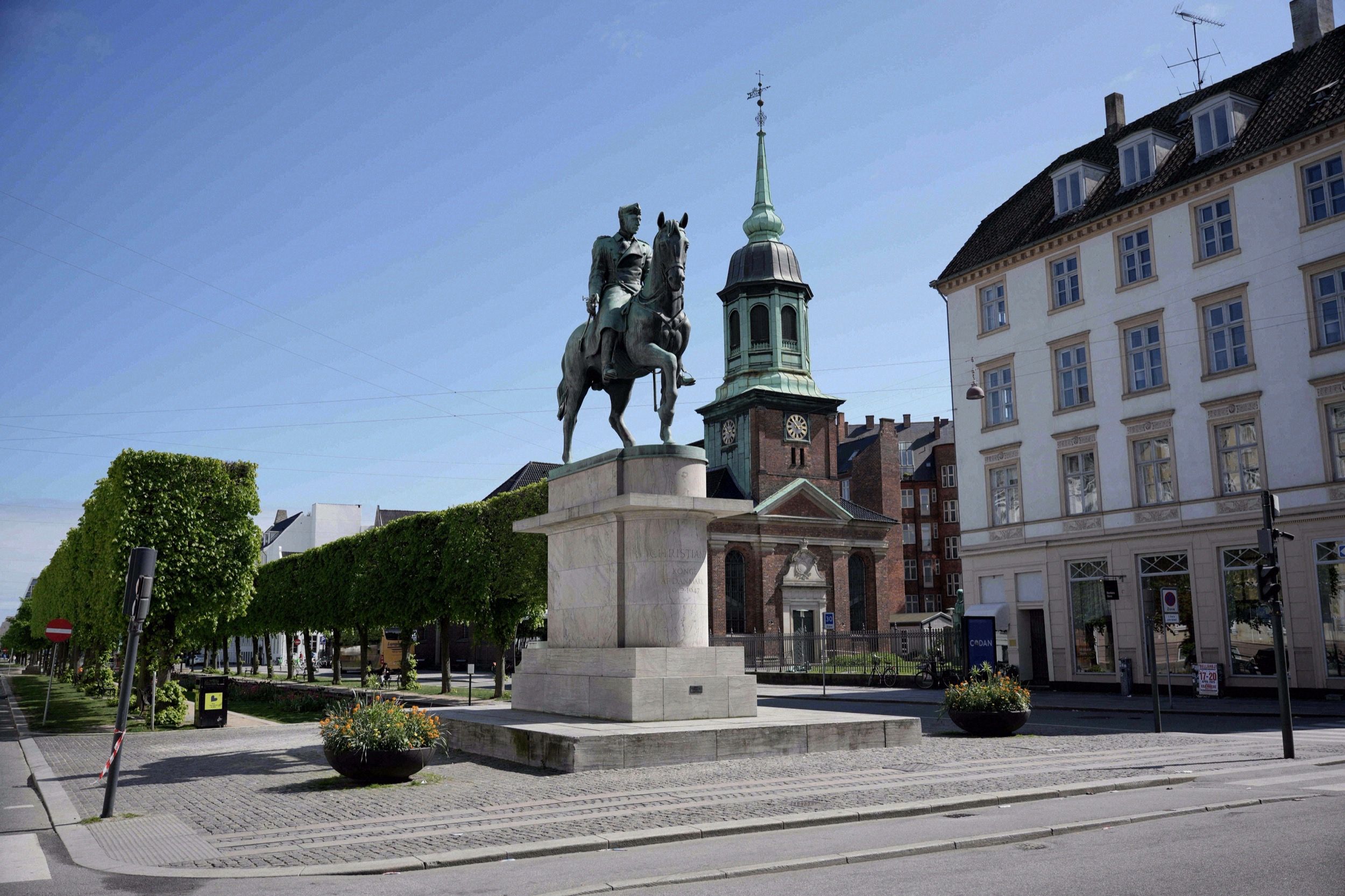 Reiterstatue Christians V. auf dem Kongens Nytorv mit Baumreihe und einer barocken Kirche im Hintergrund.