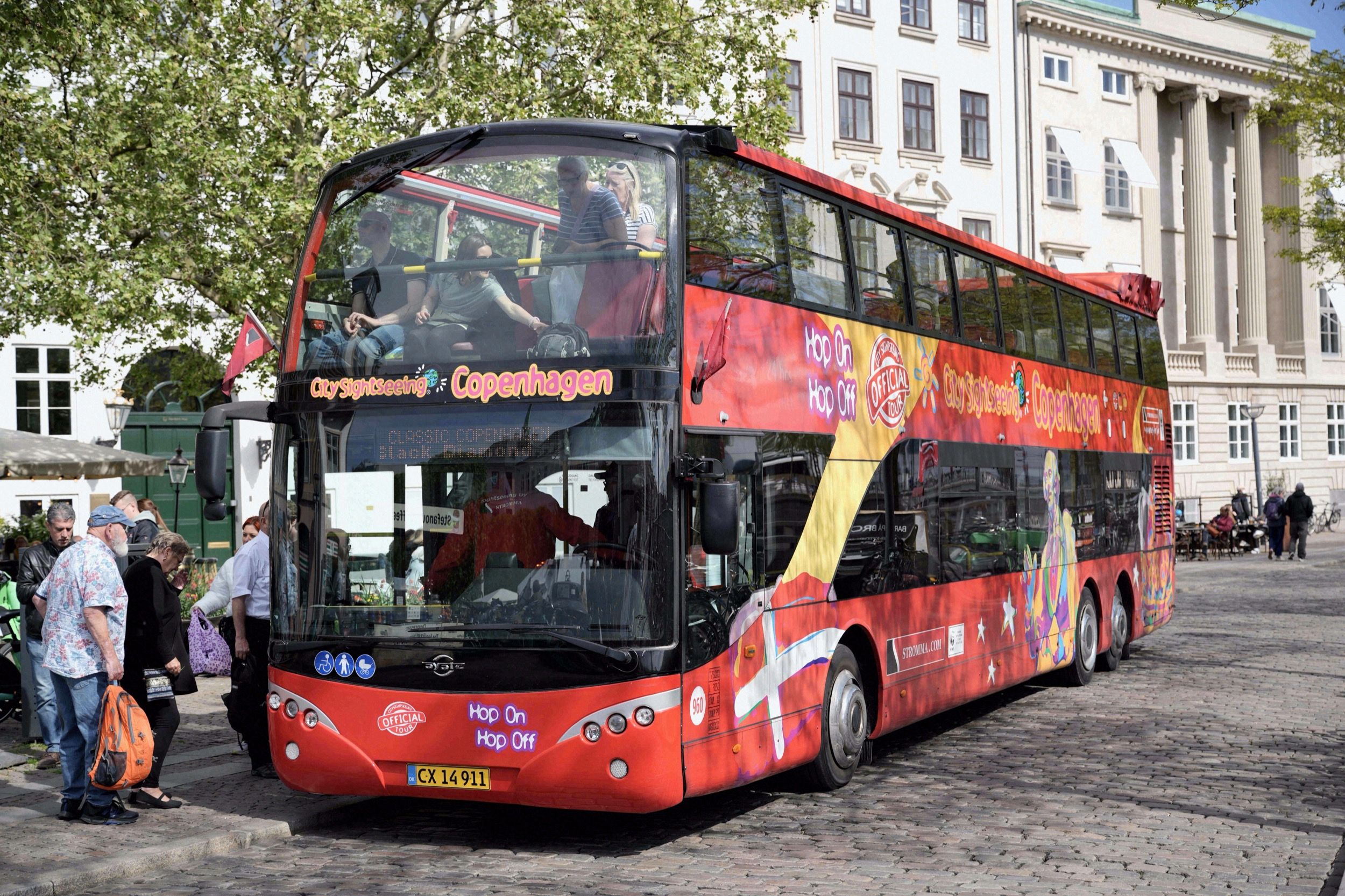 Ein roter Hop-on-Hop-off-Doppeldeckerbus von City Sightseeing Copenhagen haelt an einem belebten Platz in der Innenstadt.