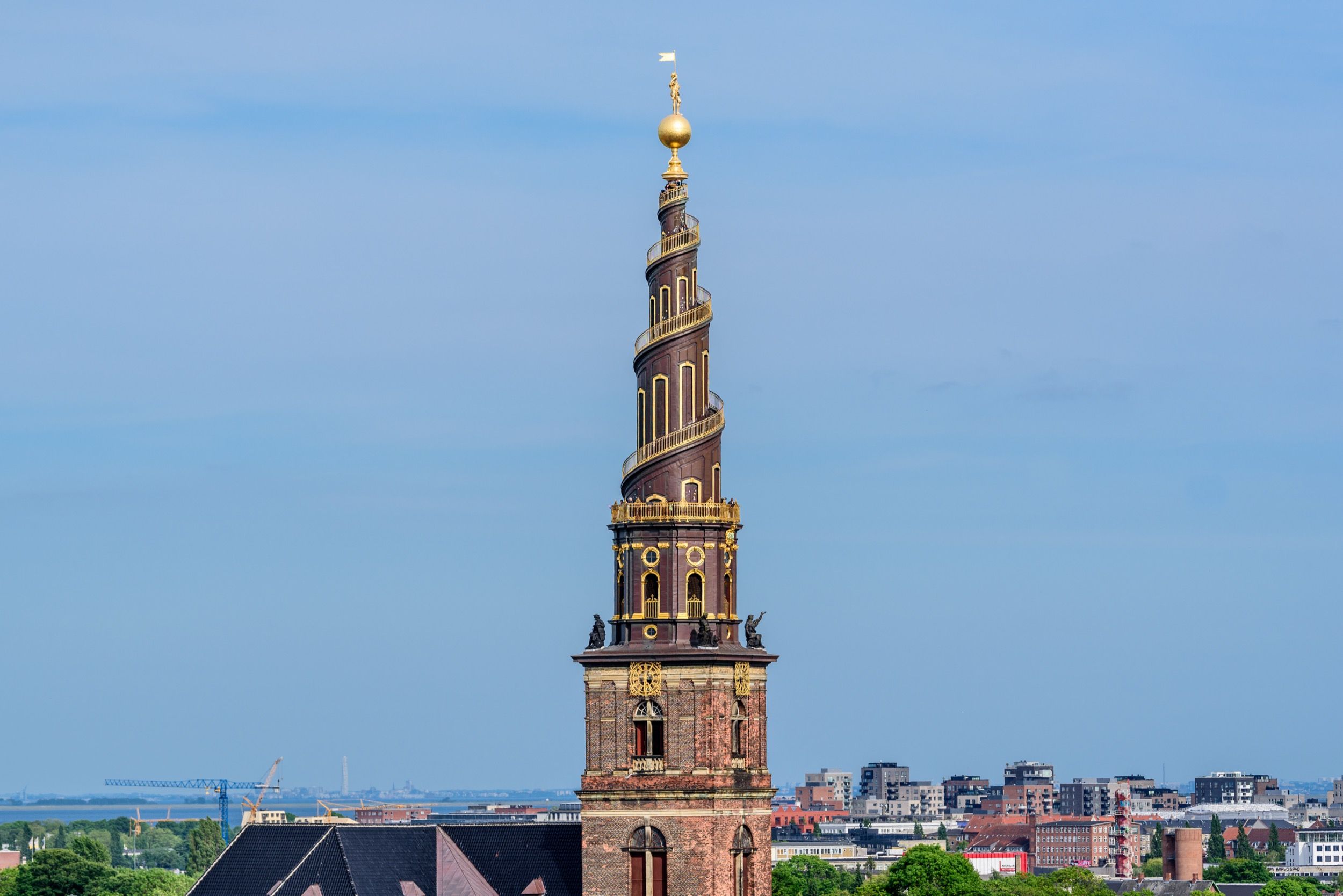 Der markante Spiralturm der Vor Frelsers Kirke in Christianshavn mit goldener Figur auf der Spitze vor blauem Himmel.