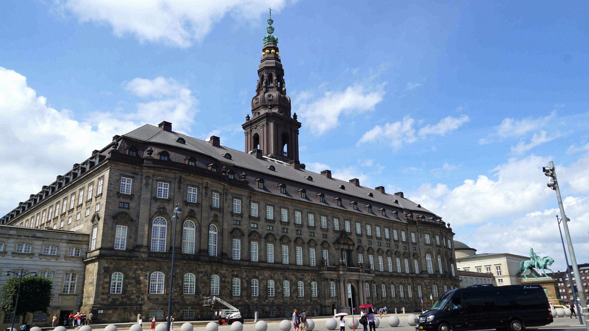 Imposing facade of Christiansborg Palace with its distinctive tower and an equestrian statue to the side.